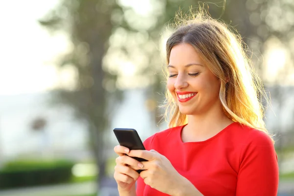 Fille en rouge textos dans un téléphone intelligent à l'extérieur — Photo