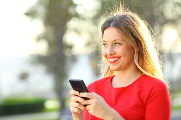 Счастливая девушка смотрит в сторону держа смартфон — стоковое фото
