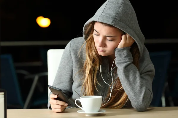 Triste adolescente ouvindo música com um telefone inteligente e fones de ouvido — Fotografia de Stock