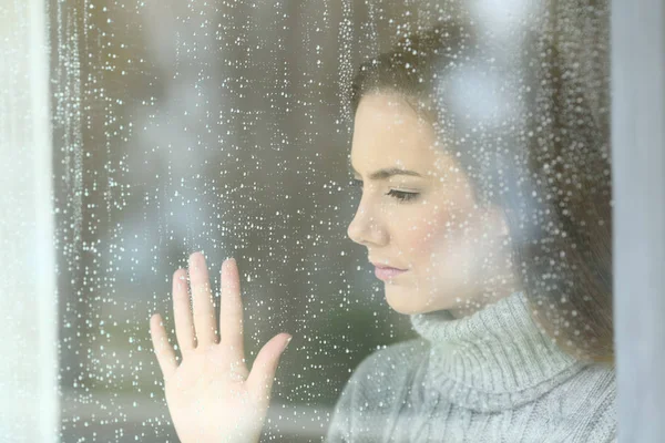 Sad girl looking through a window in a rainy day — Stock Photo, Image