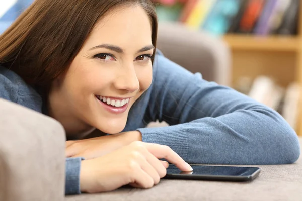 Girl using a mobile phone and looking at you at home — Stock Photo, Image