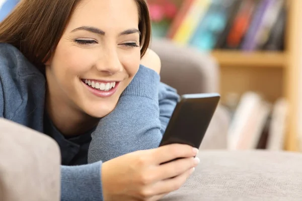 Menina usando um telefone inteligente em um sofá em casa — Fotografia de Stock