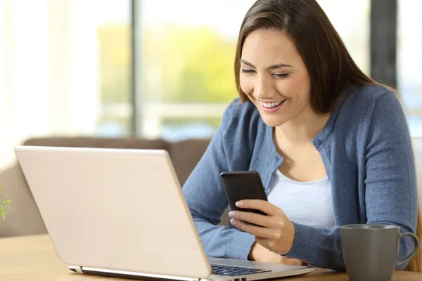 Kvinna med en telefon och en bärbar dator sitter hemma — Stockfoto