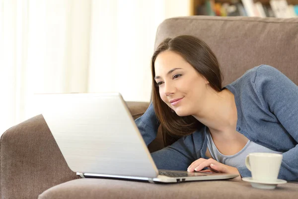 Vrouw met behulp van een laptop liggend op een bank thuis — Stockfoto