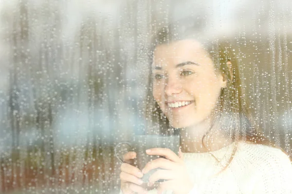 Adolescente positiva mirando a través de una ventana en un día lluvioso — Foto de Stock