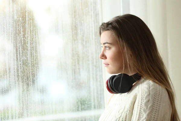 Trauriger Teenager mit Kopfhörern, der durch ein Fenster schaut — Stockfoto