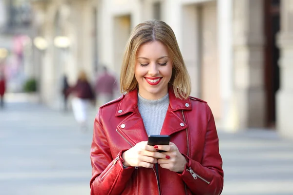 Модная блондинка ходит и пользуется смартфоном — стоковое фото