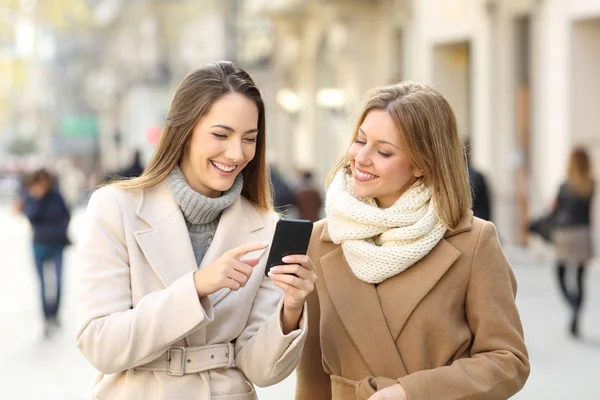 Vrienden kijken telefoon inhoud in de winter op straat — Stockfoto