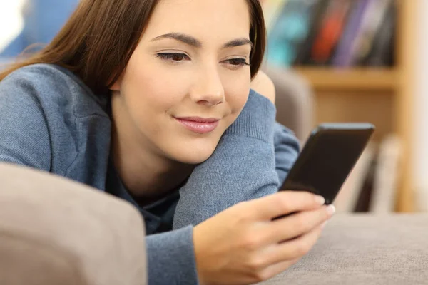 Chica leyendo el contenido del teléfono móvil en un sofá — Foto de Stock