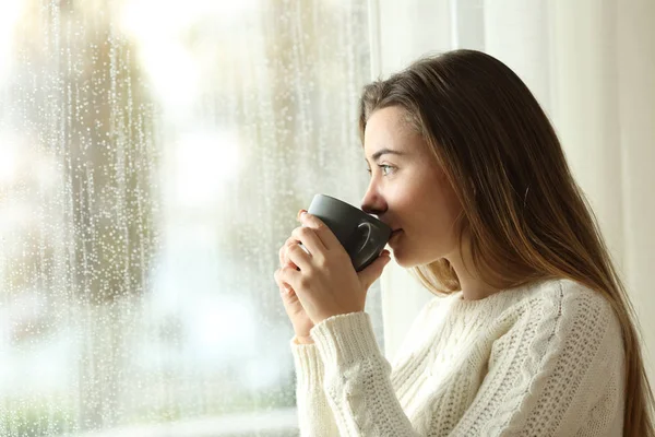 Adolescente beber café olhando através de uma janela um dia chuvoso — Fotografia de Stock