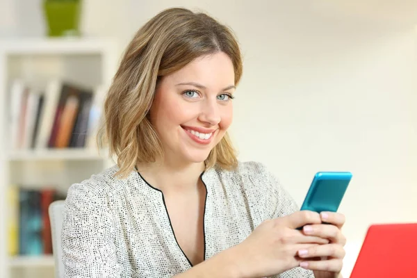 Menina satisfeita segurando um telefone inteligente olhando para você — Fotografia de Stock