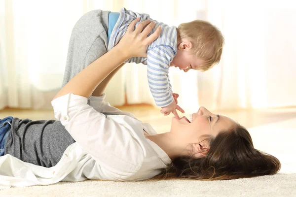 Lycklig mamma på golvet att höja hennes baby son — Stockfoto