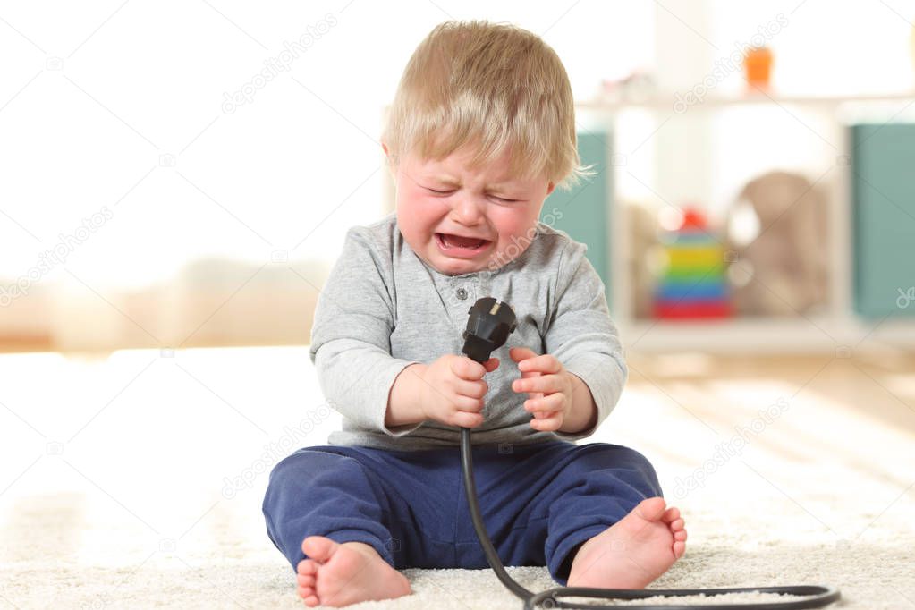 Baby crying holding an an electric plug