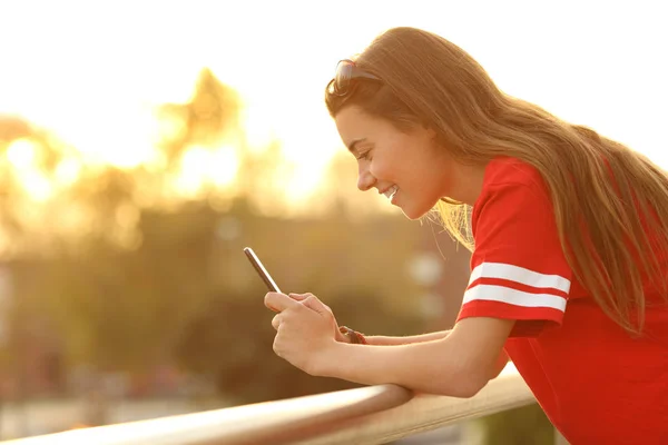 Profil av en tonåring som håller en smart telefon i en balkong — Stockfoto