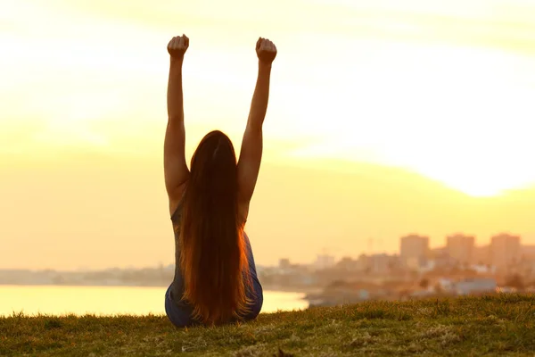 Opgewonden vrouw verhogen armen kijken naar de zonsondergang over de stad — Stockfoto