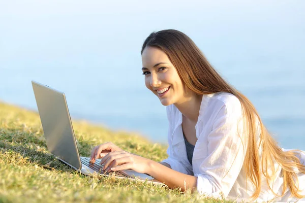 Mujer feliz usando un portátil en la hierba mirándote — Foto de Stock