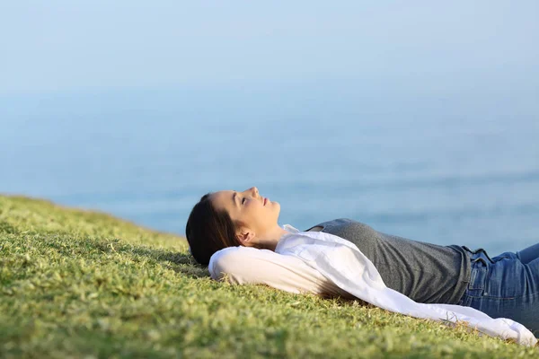 Mujer relajada descansando sobre la hierba en la costa —  Fotos de Stock