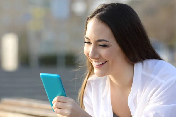 Smiley adolescent à l'aide d'un téléphone intelligent bleu dans la rue — Photo