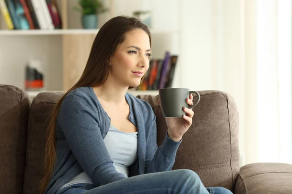 Mulher bebendo café e olhando para um sofá — Fotografia de Stock
