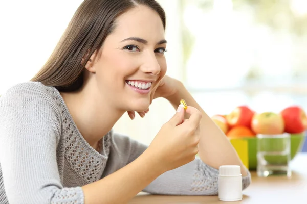 Woman taking a vitamin pill and looking at you at home — Stock Photo, Image