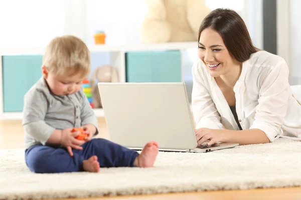 Mor som arbetar med en bärbar dator och baby spelar — Stockfoto