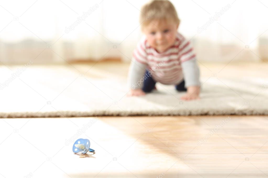 Baby crawling towards a dirty pacifier on the floor