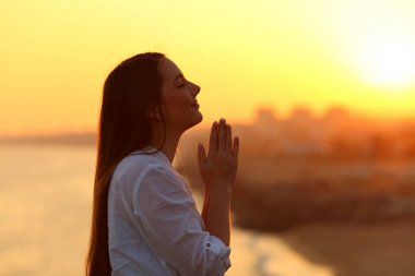 Profile of a woman praying at sunset clipart
