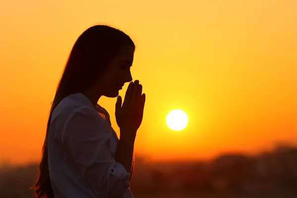 Backlight de uma mulher orando ao pôr do sol — Fotografia de Stock