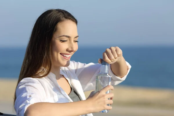 Chica opeining una botella de agua en la playa —  Fotos de Stock