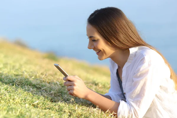 Mujer feliz usando un teléfono inteligente tumbado en la hierba — Foto de Stock
