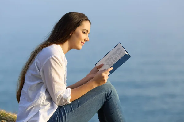 Расслабленная женщина читает книгу, сидя на пляже — стоковое фото