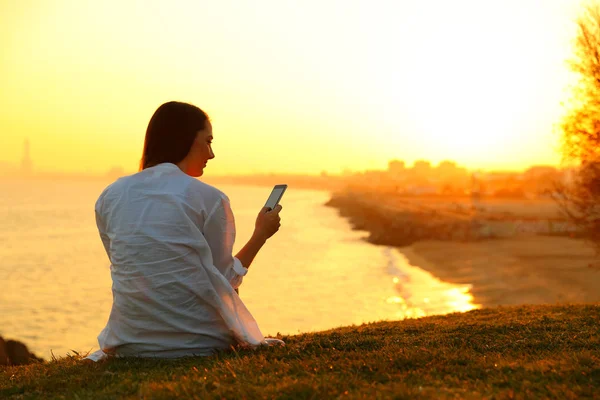 Mulher solteira usando um telefone inteligente ao pôr do sol — Fotografia de Stock