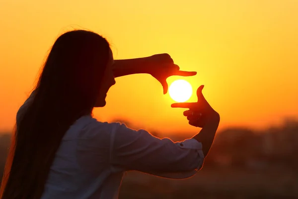 Vrouw framing zon met vingers bij zonsondergang — Stockfoto