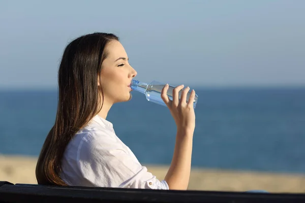 Donna che beve acqua da una bottiglia sulla spiaggia — Foto Stock