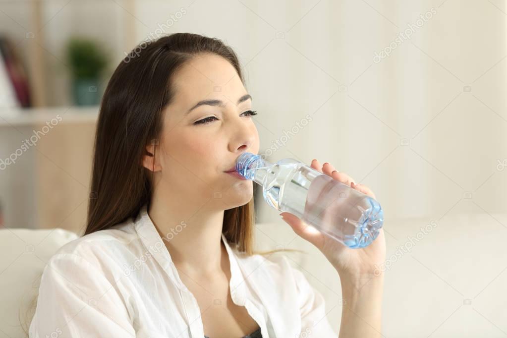 Woman drinking water from a bottle at home