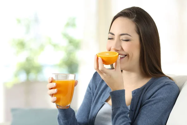 Mulher cheirando uma laranja e segurando um suco — Fotografia de Stock