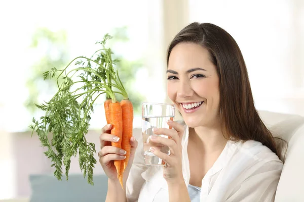 Mulher segurando cenouras e um copo de água olhando para a câmera — Fotografia de Stock