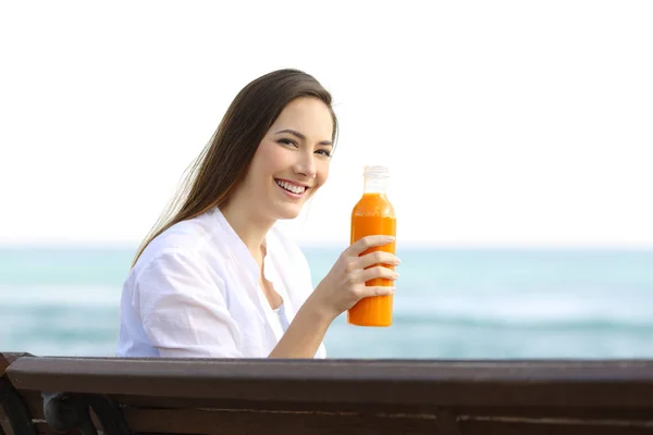 Mujer sosteniendo una botella de jugo de naranja en la playa — Foto de Stock