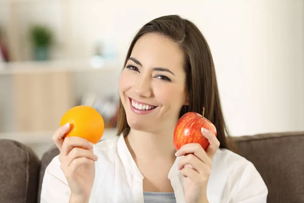 Женщина, держащая яблоко и апельсин, смотрит в камеру — стоковое фото