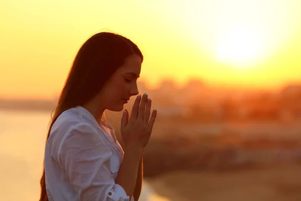 Vista lateral de una mujer rezando al atardecer — Foto de Stock