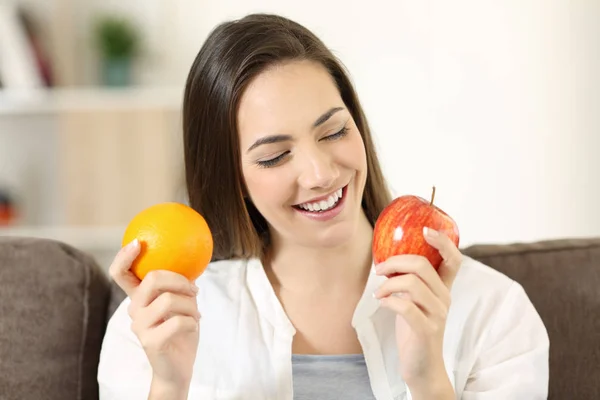 Nainen päättää appelsiinin ja omenan välillä kotona — kuvapankkivalokuva