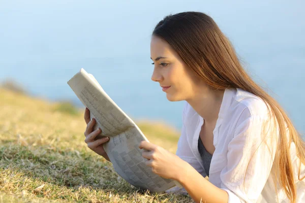 Meisje het lezen van een krant op het gras — Stockfoto