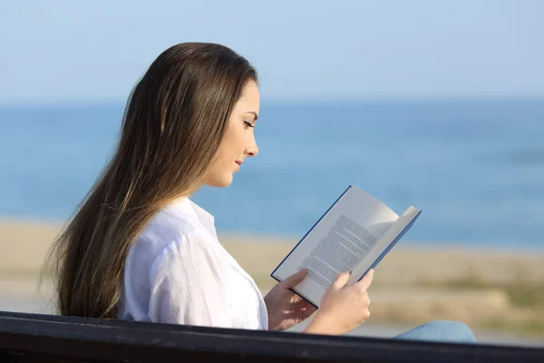 Frau liest ein Buch auf einer Bank am Strand — Stockfoto