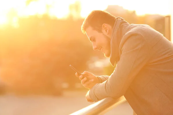 Homem feliz usando um smartphone no inverno ao pôr do sol — Fotografia de Stock