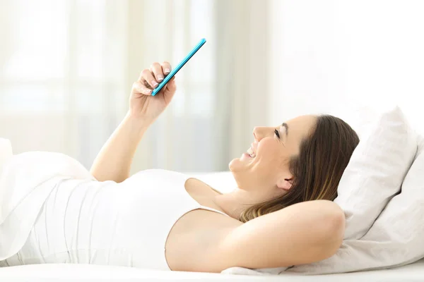 Профиль женщины, использующей смартфон на кровати — стоковое фото