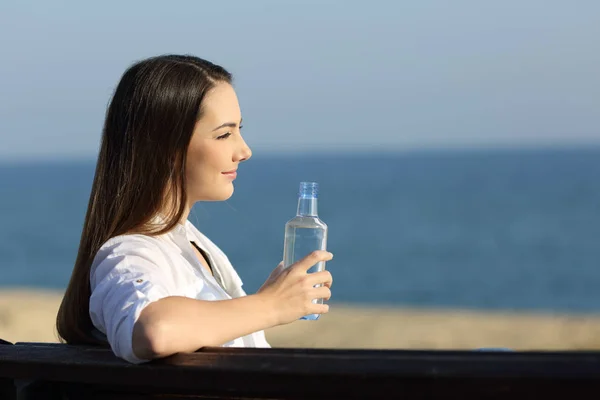 Smiley kvinna innehar en vattenflaska på stranden — Stockfoto