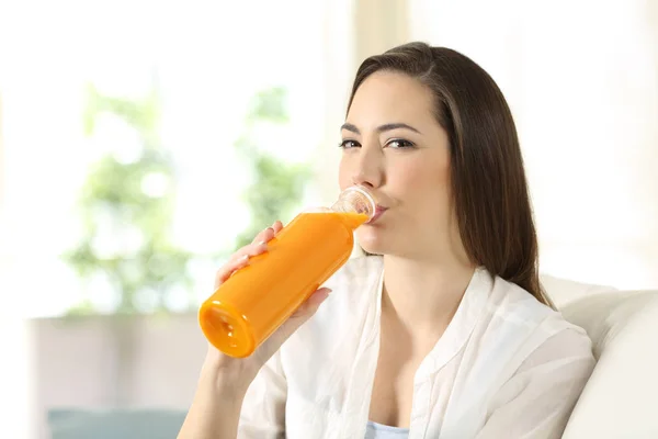 Mujer bebiendo jugo de naranja de una botella mirándote — Foto de Stock