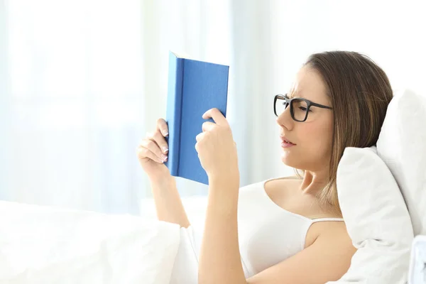 Mujer leyendo un libro con anteojos en la cama —  Fotos de Stock
