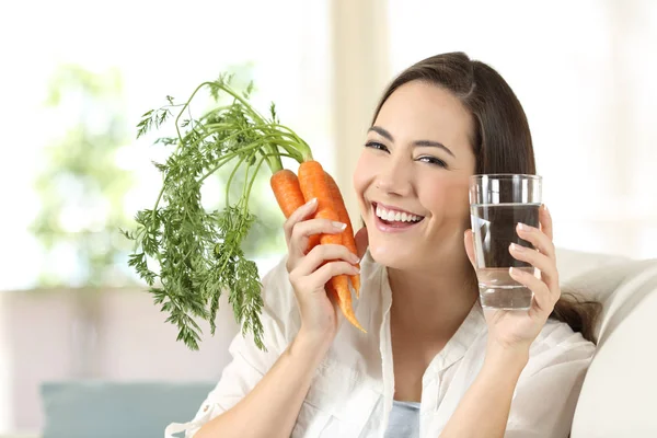 Mujer mostrando zanahorias saludables y vaso de agua — Foto de Stock