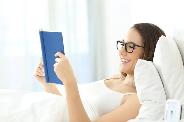 Mulher usando óculos lendo um livro na cama — Fotografia de Stock
